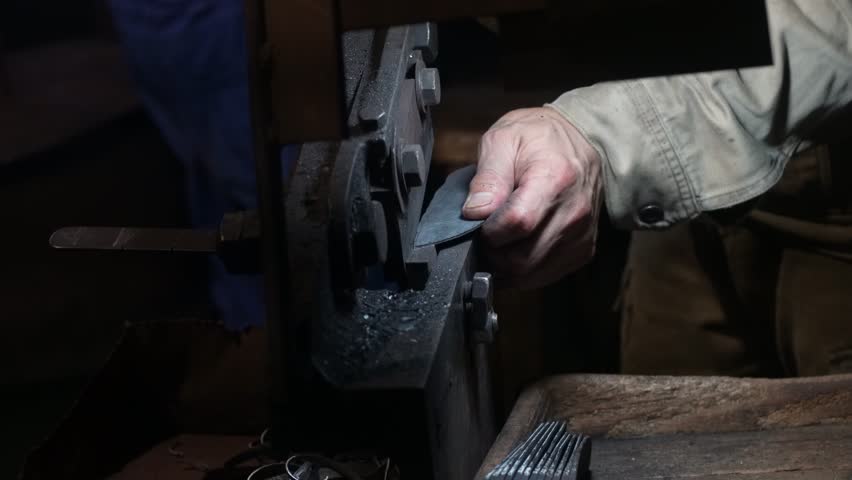 A craftsman uses a hand shear to cut the material into the shape of a knife