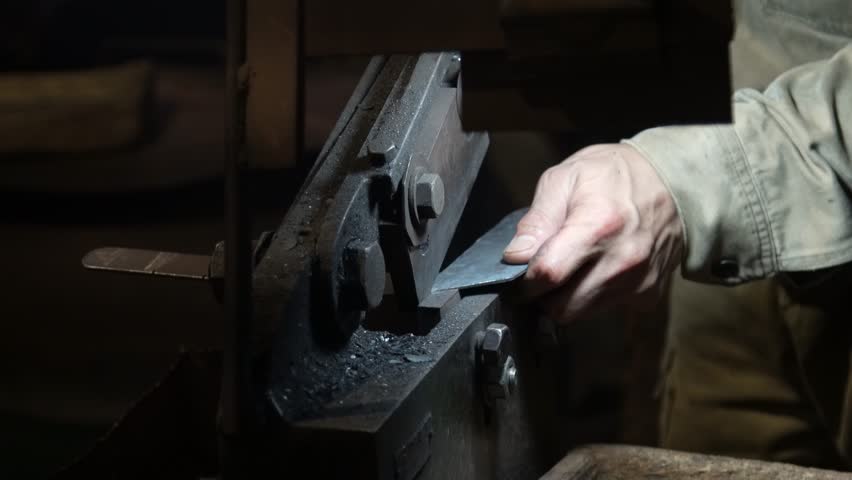 A craftsman uses a hand shear to cut the material into the shape of a knife