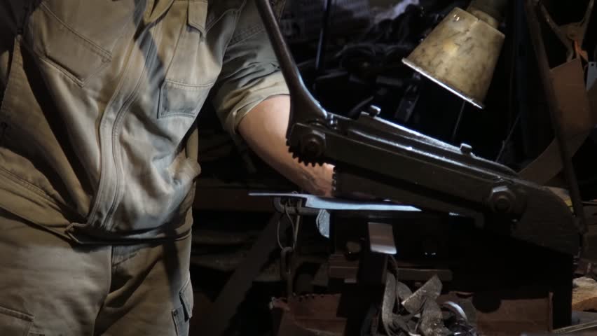 A craftsman uses a hand shear to cut the material into the shape of a knife
