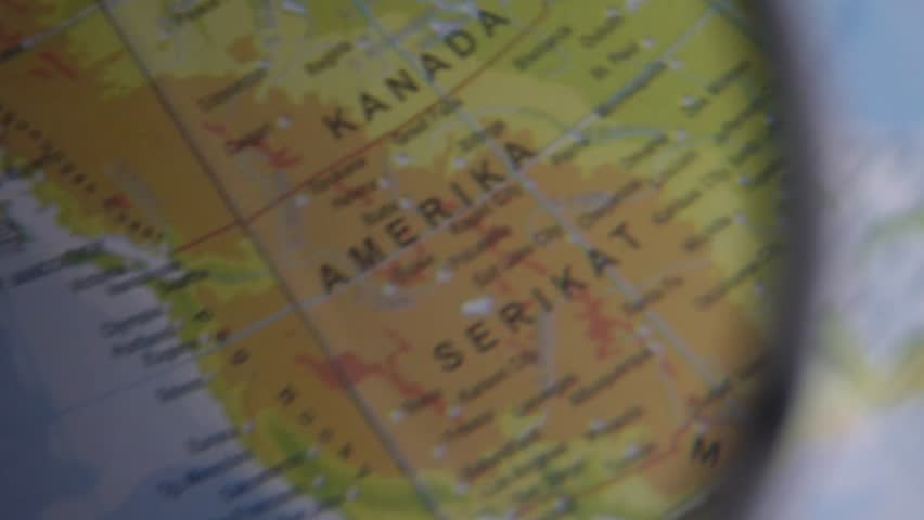 The Americas are seen through a magnifying glass. The image of a hand holding a magnifying glass shows the North America on a globe.