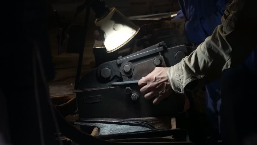 A craftsman uses a hand shear to cut the material into the shape of a knife