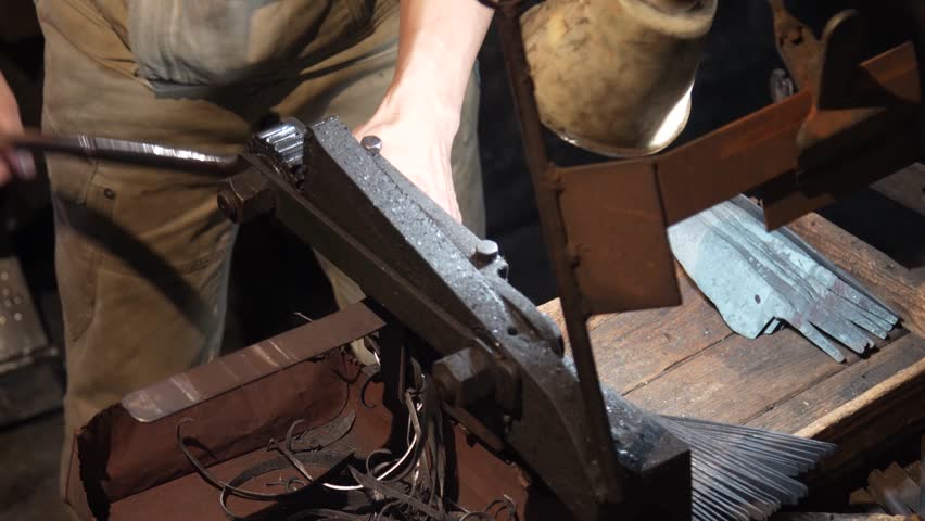 A craftsman uses a hand shear to cut the material into the shape of a knife