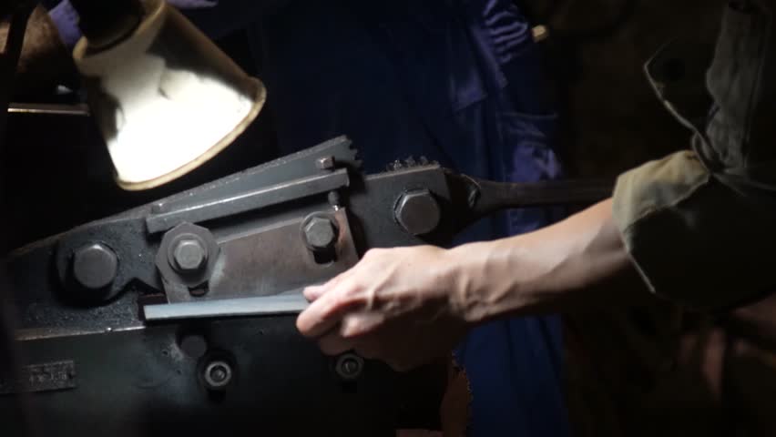A craftsman uses a hand shear to cut the material into the shape of a knife