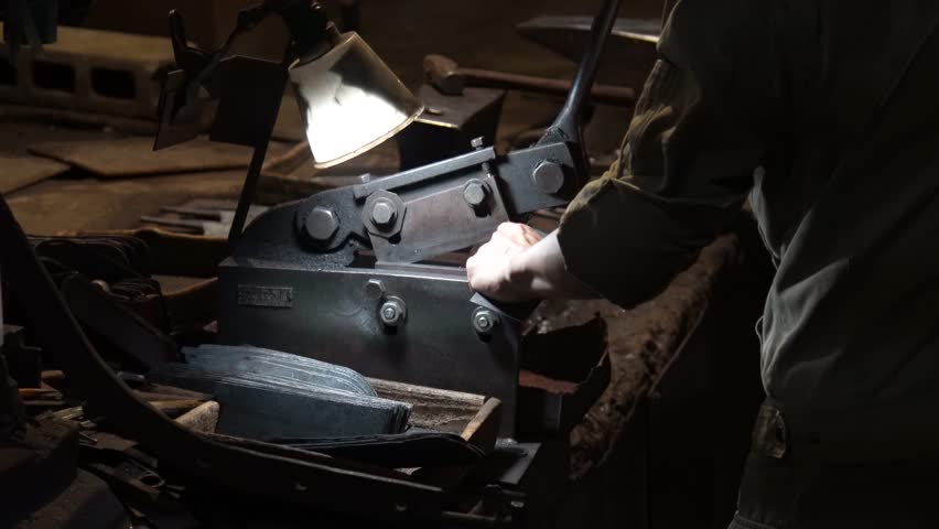 A craftsman uses a hand shear to cut the material into the shape of a knife