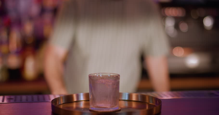Cocktail bar. Preparing alcohol drink. Barman pouring liquor liquid from bottle to metal shaker. Wide crystal glass with big ice cube.
