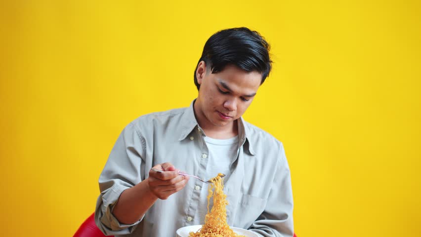 Casual young man reacts to spiciness while trying eat noodles isolated on yellow background