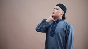 Young Muslim man praying with eyes closed and hand on neck seeking divine connection and peace. Doing Adzan - Powered by Shutterstock - Get 15% off with code: PIKWIZARD15