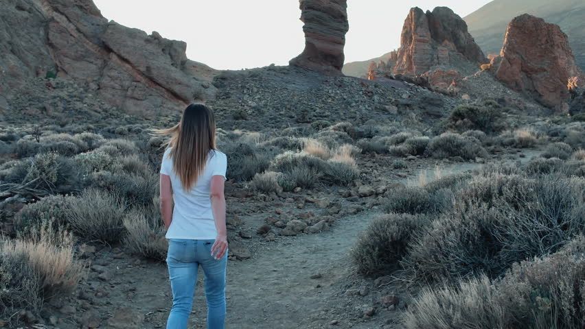 A woman walks towards Roque Cinchado in Teide National Park during sunset.