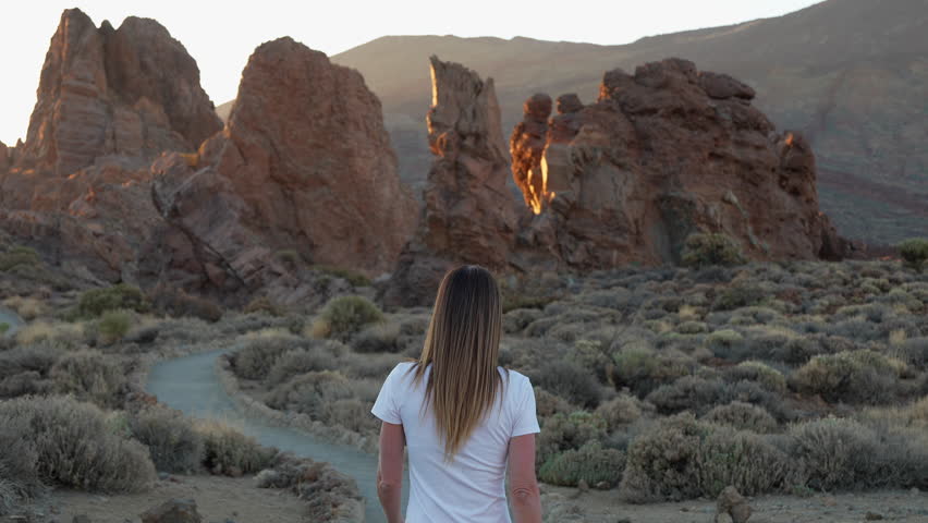 Woman walking towards Roque Cinchado at sunset in Teide National Park
