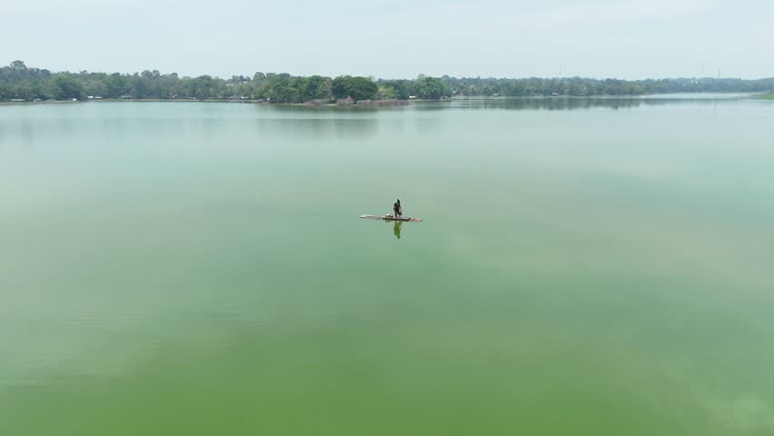 Aerial view of fisherman casting net from traditional raft on tranquil lake