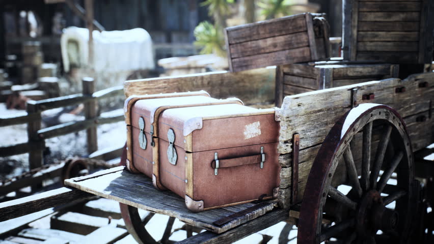 A rustic wooden cart is filled with worn leather suitcases, resting in a dusty old western town. The scene evokes a sense of travel and adventure from a bygone era.
