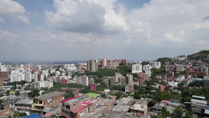 Daytime drone panning shot of Cali Valle del Cauca Colombia showing the city under bright midday sun with urban skyline and surrounding mountains.
