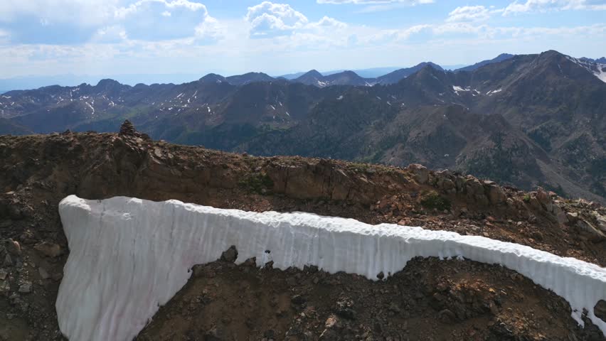 Hiker hiking walk down past cairn 14er summit Mount of the Holy Cross peak Sawatch Range Colorado aerial drone Rocky Mountains spring summer snow field cornice chute blue sky Elk Mountains view
