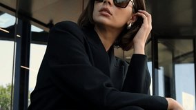 Stylish woman with sunglasses posing against a modern building with large smoky glass windows and concrete walls. Close up of legs walking down steps, wearing leather pants or dress. Fashion ad. - Powered by Shutterstock - Get 15% off with code: PIKWIZARD15