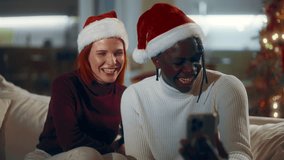 Pair of bloggers recording video congratulations for followers in Christmas. African American man and Caucasian woman in Santa hats looking at frontal camera of smartphone in decorated living room - Powered by Shutterstock - Get 15% off with code: PIKWIZARD15