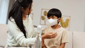 Asian mother gently puts protective face mask on young son in bright living room. - Powered by Shutterstock - Get 15% off with code: PIKWIZARD15