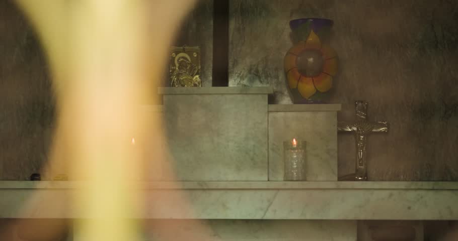 Two urns sit in a traditional white marble Mexican tomb with candles lit for Dia de los Muertos. Catholic imagery surrounds it. Mexico City.