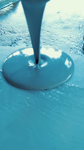 Construction worker pours blue epoxy resin on floor and spreads it with a trowel