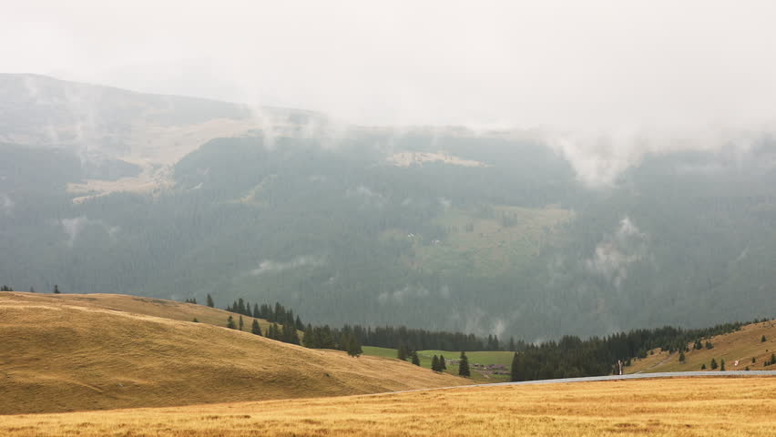 Mountain landscape on a rainy day with cloudy sky, lake and forest of conifers. View from the car with raindrops on the mirror, fog over hills, rocks and pine branch on stone.