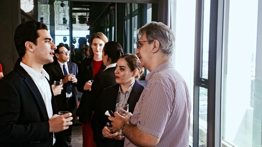 Professionals in business attire chat by large windows with drinks at office event. Corporate mixer blends networking, teamwork, meeting, seminar, workshop, conference, reception, and meetup.