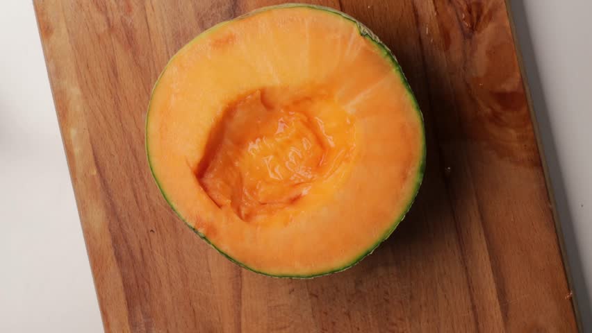 Slicing orange melon into thin wedges on wooden cutting board. Close-up of hands preparing fresh fruit in home kitchen for healthy snack or meal prep