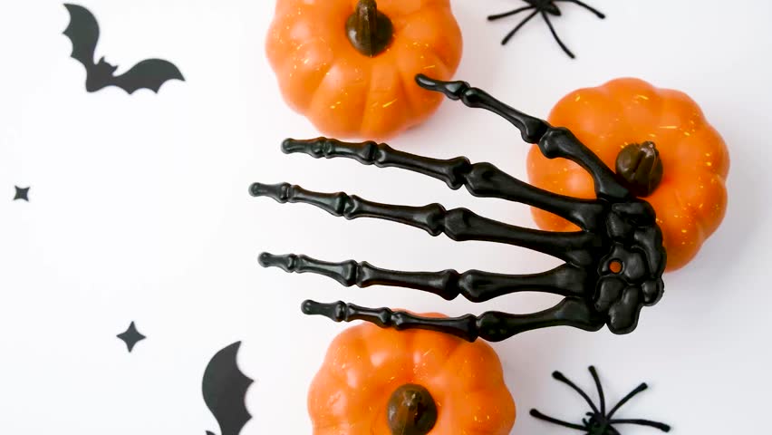 Black skeleton hand reaching for small orange pumpkins with bats and a spider