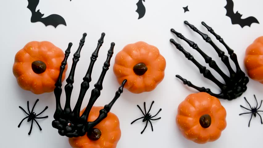 Black skeleton hands grab orange pumpkins with small black spiders and bats on white background