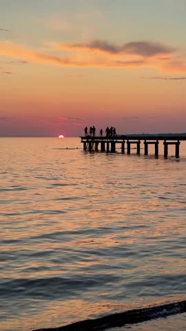 Sunset seascape with dramatic clouds, ocean waves, and a wooden pier. Warm reflections on the beach create a peaceful and atmospheric mood