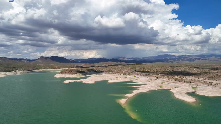 Aerial view of the tranquil Lake Pleasant shoreline meeting the arid landscape under a sky of dramatic clouds, Lake Pleasant, Arizona, United States.