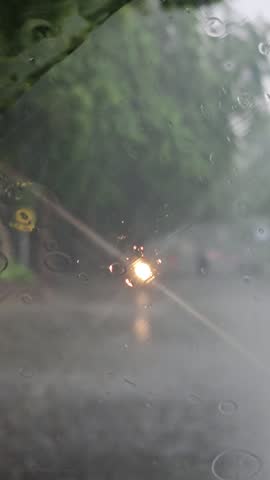​A captivating POV shot from inside a car navigating a heavy rainstorm on a city street at night. The wipers struggle against the torrent, and the distant streetlights blur into streaks of light.