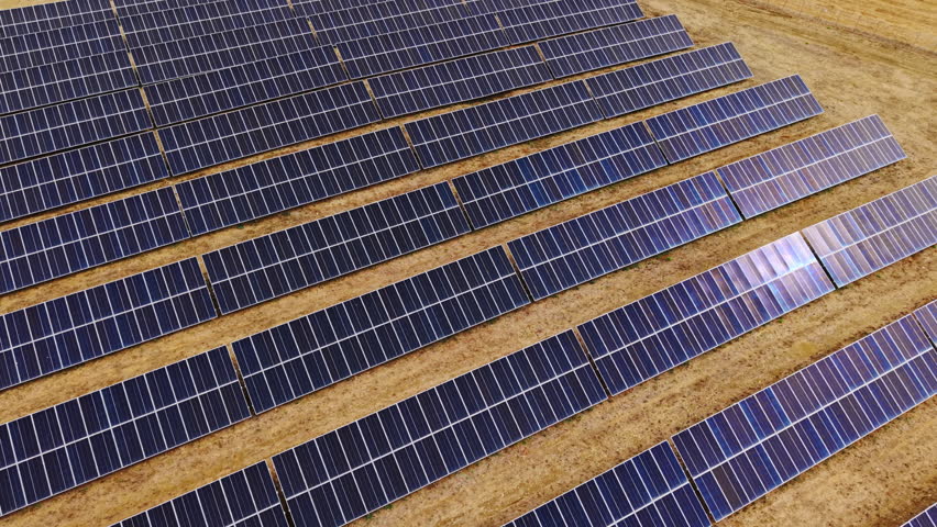 Drone descends in total top-down view, approaching a wide field of photovoltaic solar panels installed on dry soil in Sicily.