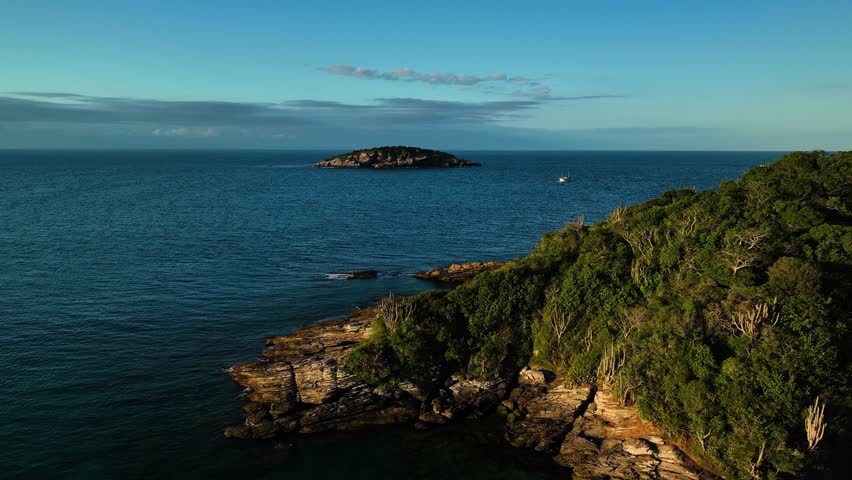 Aerial view of the rugged, rocky coastline meets the deep blue sea, with a small island visible in the distance, Paraty, State of Rio de Janeiro, Brazil.