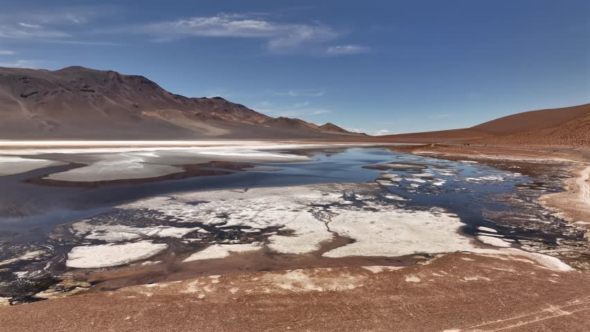 Aerial view of the stark landscape of Ruta 27 with its contrasting water and salt textures, reflecting the arid beauty of the mountains, Salar y Laguna de Tara, Antofagasta, Chile.