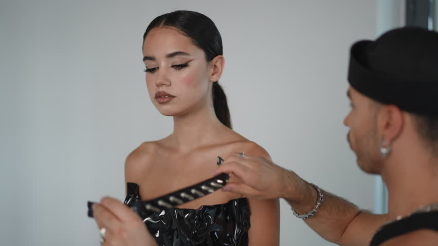 A stylist prepares a stunning model in a glossy dress with an edgy choker, enhancing her beauty in a modern setting