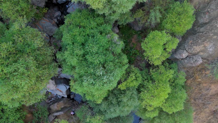 Aerial view of a small waterfall cascading into a natural rock pool surrounded by rugged cliffs and sparse vegetation. Herher Waterfall