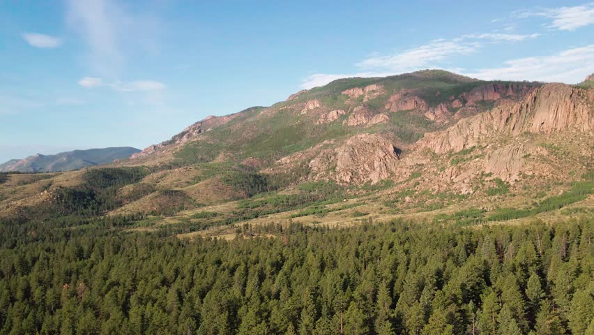 A panning drone flight over a remote mountain forest with wilderness area and rocky cliffs in the distance. Filmed in the Pike National Forest of Colorado.