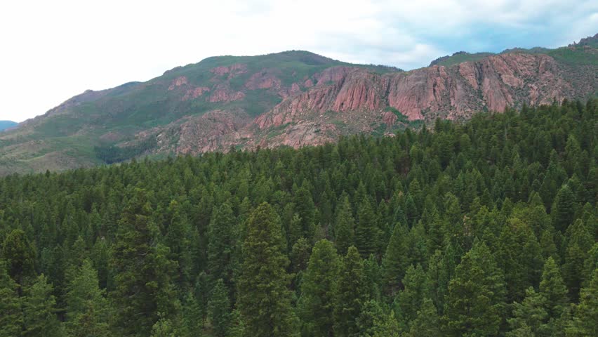Aerial view approaching remote red cliffs over a pine forest. Filmed with a drone in the Pike National Forest.