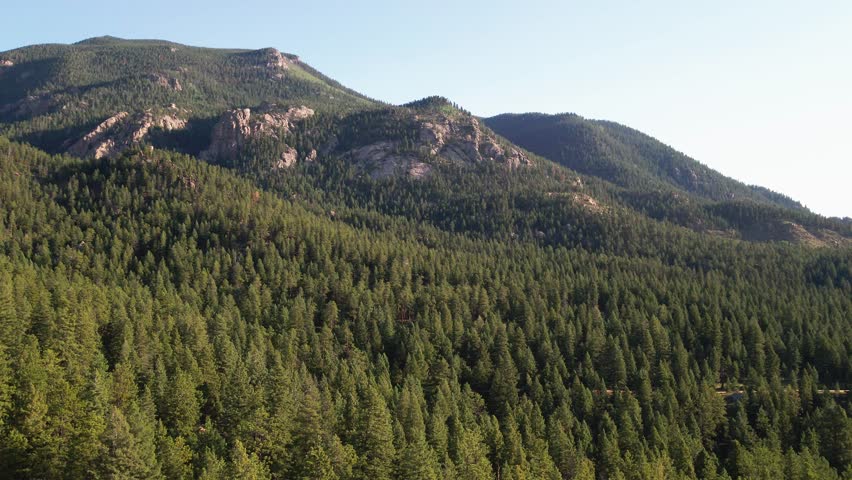 A slow drone flight over a remote mountain forest with wilderness area and rocky cliffs in the distance. Filmed in the Pike National Forest of Colorado.