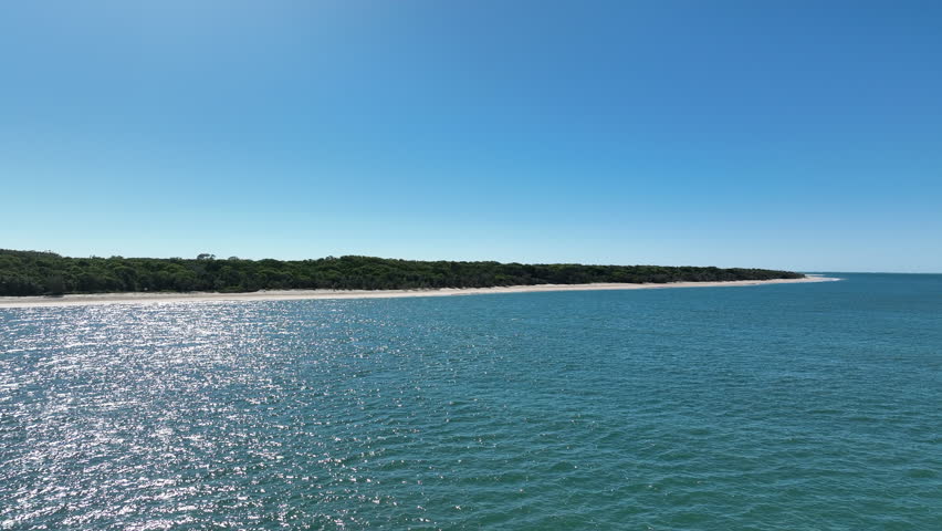 Low flight over the Great Sandy Strait towards the densely vegetated southern tip of K'gari Fraser Island on a perfect blue calm day. Queensland Australia.