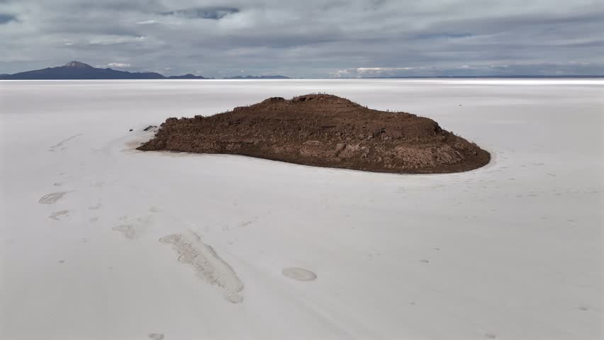 Aerial view of land contrasting starkly against the bright, expansive salt flat under a cloudy sky, Salar de Uyuni, Potosi Department, Bolivia.