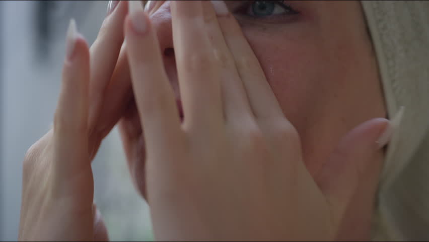 Young pretty woman applying moisturizer on her face during daily self care skincare treatment, close up shot. Beauty maintenance routine concept.