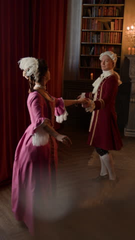 Vertical shot of young Caucasian noble lord in frock coat and breeches and lady in Victorian style dress performing courteous menuet dance during party or ball in palace hall