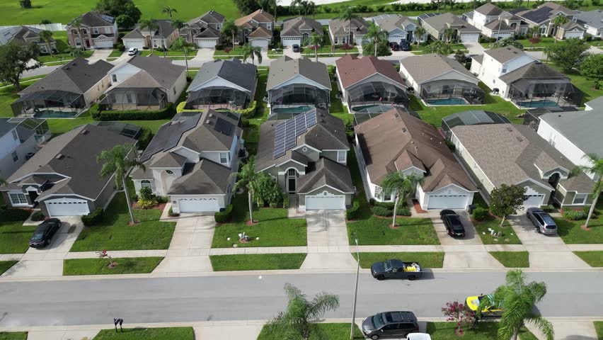 Drone circles a modern house in Kissimmee, Florida, featuring rooftop solar panels and a private backyard pool. Sunny skies and a suburban neighborhood complete this aerial view