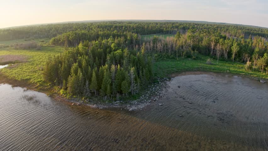 Aerial drone footage over the Les Cheneaux Islands in Michigan’s Upper Peninsula, showcasing clear blue water, forested shorelines, sandy spits, and sailboats in the evening light.