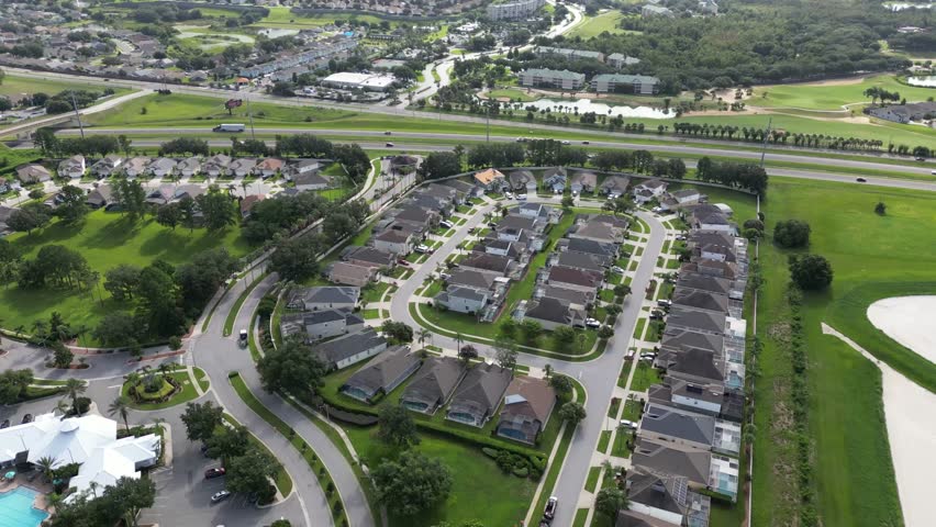 Aerial drone footage showcasing a wide circling view over a residential neighborhood in Kissimmee, Orlando, Florida. Features rooftops, roads, trees, and scenic suburban layout under blue skies