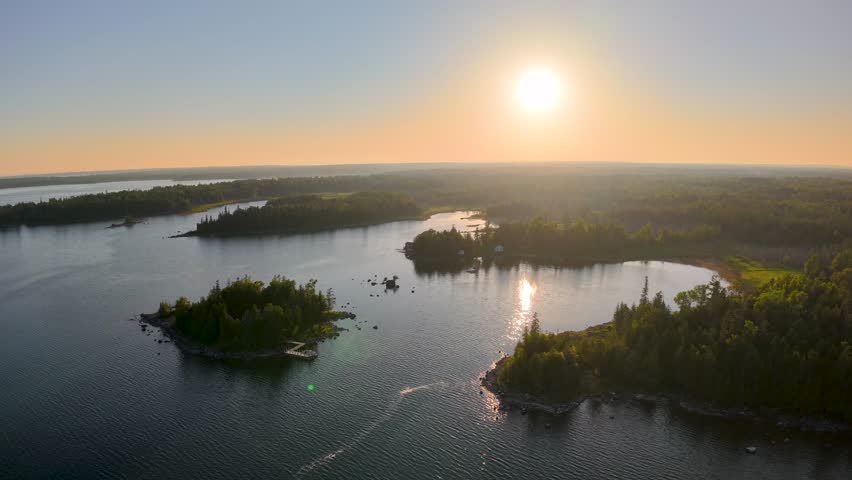 Scenic aerial drone view of Les Cheneaux Islands in Michigan’s Upper Peninsula at sunset, with golden light reflecting on calm lake waters and forested shores.