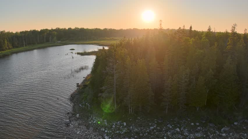 Aerial drone view of a river winding through dense forest in Michigan’s Upper Peninsula at sunset, with golden light reflecting on the water.