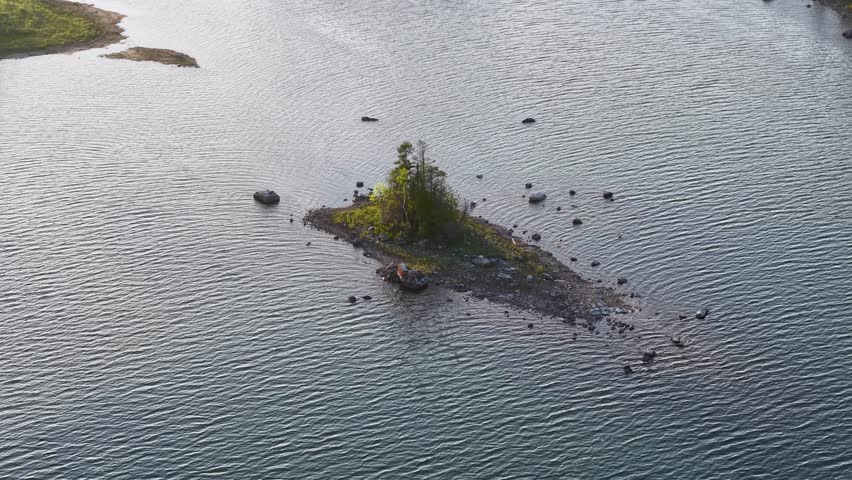 Aerial drone view of a small rocky island covered with trees surrounded by calm lake waters in Michigan’s Upper Peninsula wilderness.