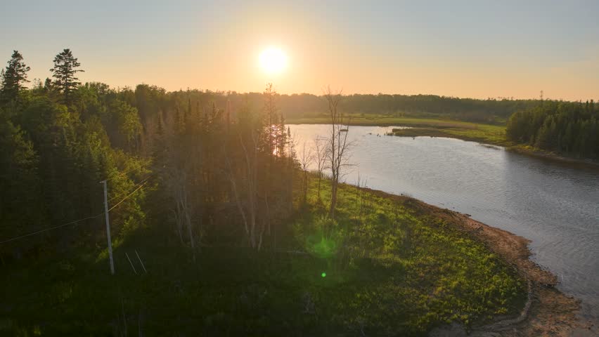 Aerial drone footage of Bald Eagle and golden sunset casting warm light over a forested shoreline and calm waters in Michigan’s Upper Peninsula, Les Cheneaux Islands.