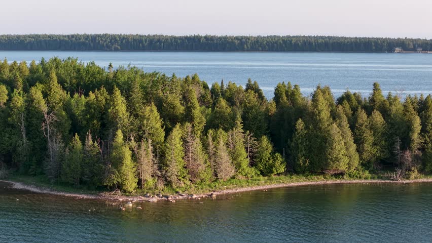 Aerial drone view of a forested shoreline along the Les Cheneaux Islands in Michigan’s Upper Peninsula with blue lake waters.